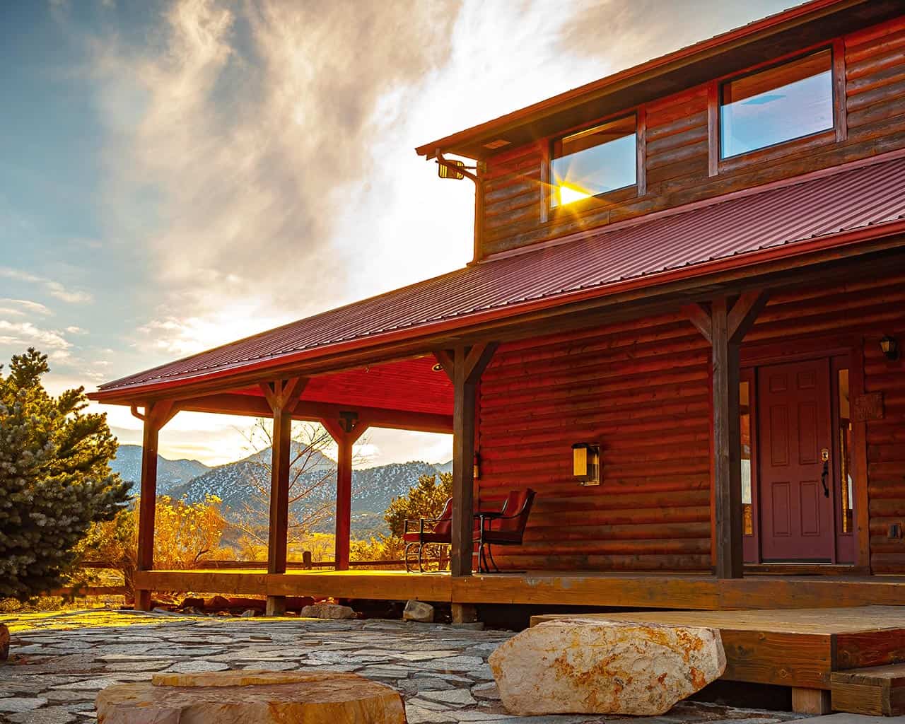 A log-style ranch home with a covered porch and mountain views at sunset