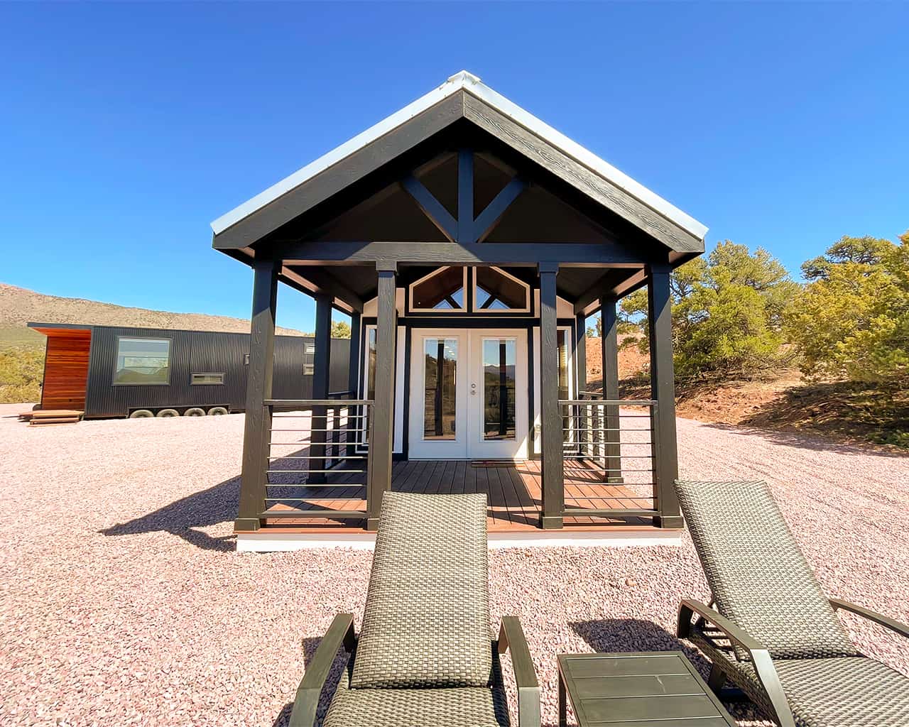 A small gabled cabin with French doors and a covered porch, two lounge chairs in front, under a clear blue sky