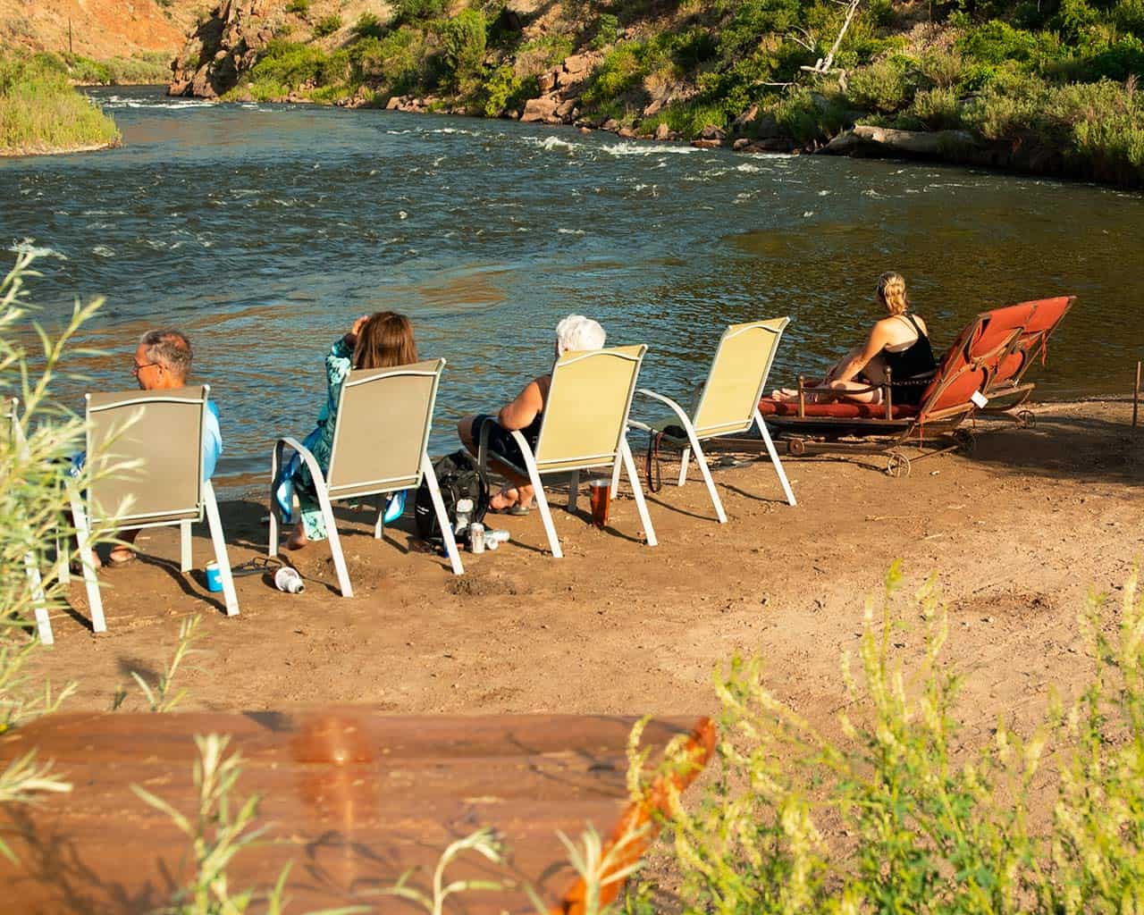 Guests relaxing in chairs on the sandy bank of the Arkansas River